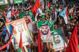 A large crowd of people carrying flags and holding signs with faces on them.